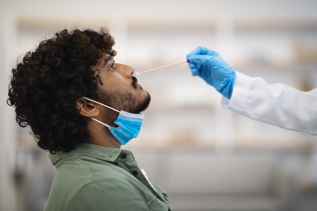 Closeup of curly Indian guy having nasal swab test at clinic, COVID-19 diagnostic testing.