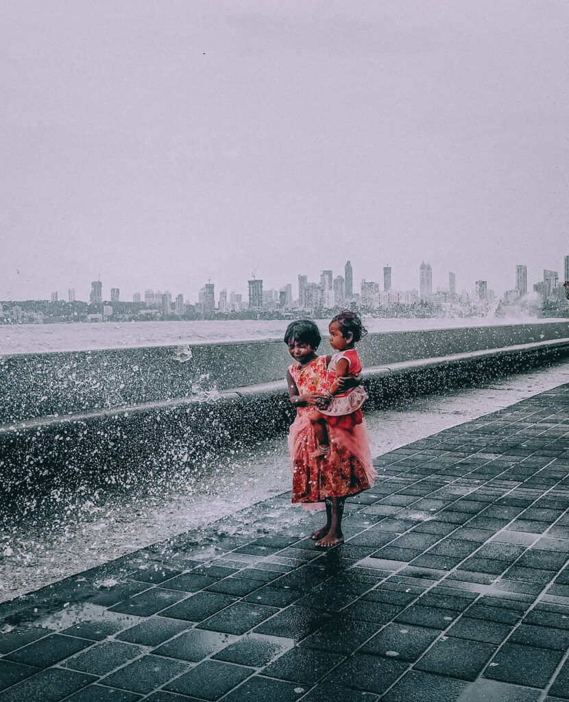 Small girl holding a kid and standing near a beach