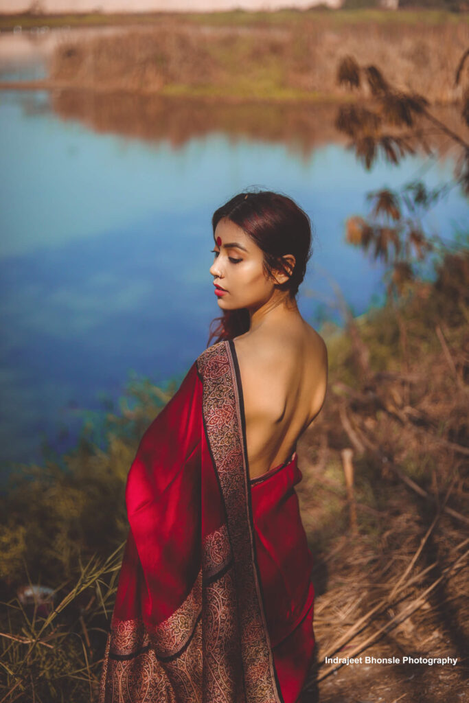 Woman wearing red saree is standing beside a lake