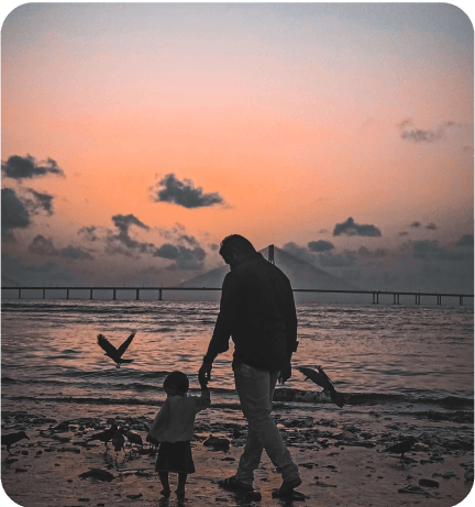 A man and a child walking on the beach at sunset.