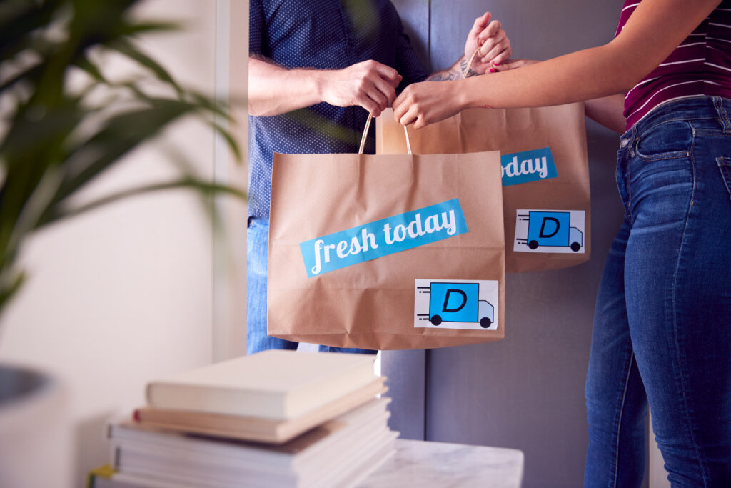 Close Up Of Home Delivery Service Driver Handing Takeaway Food Bags To Female Customer At Home